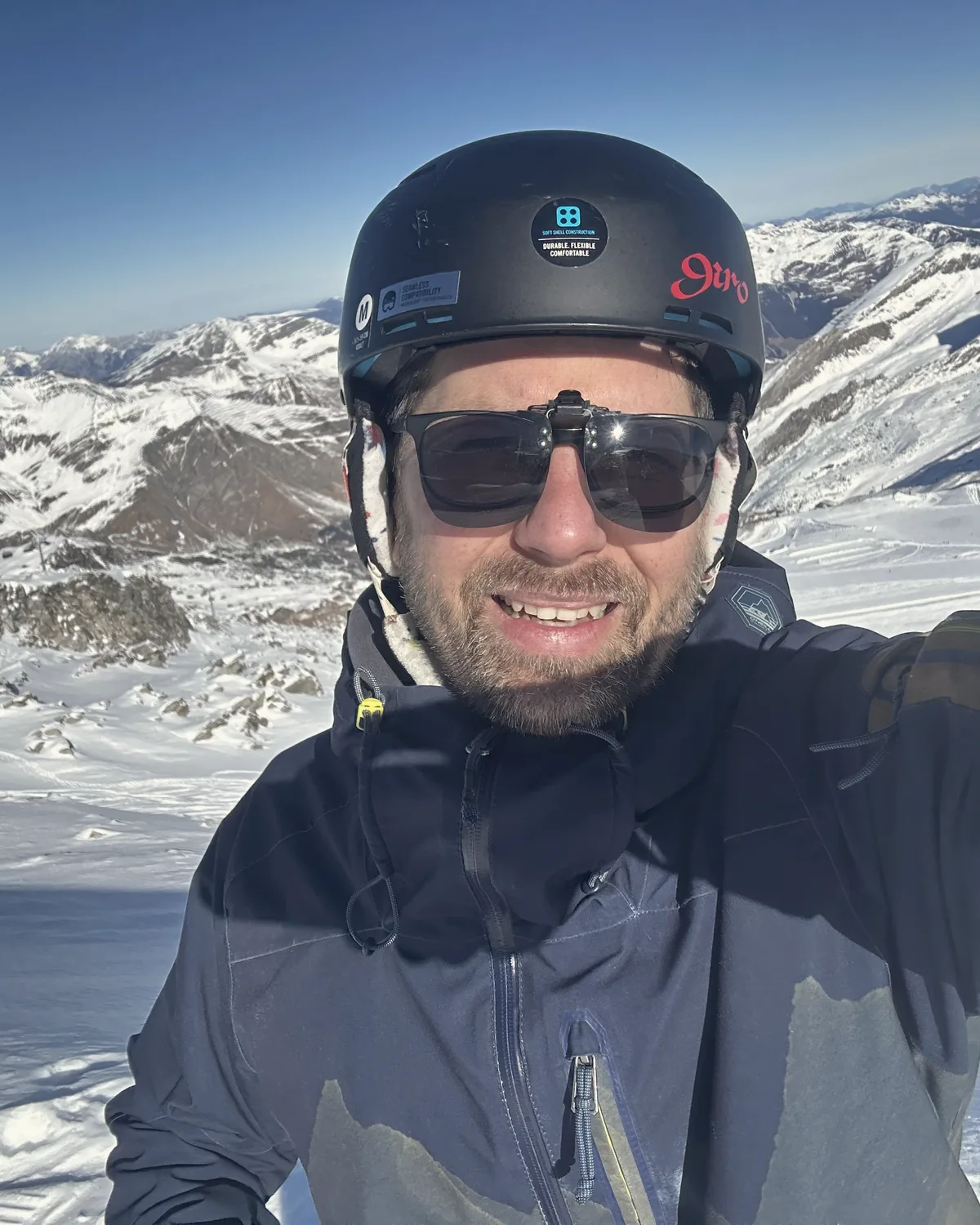Selfie mit Helm und Sonnenbrille vor verschneiten Bergen