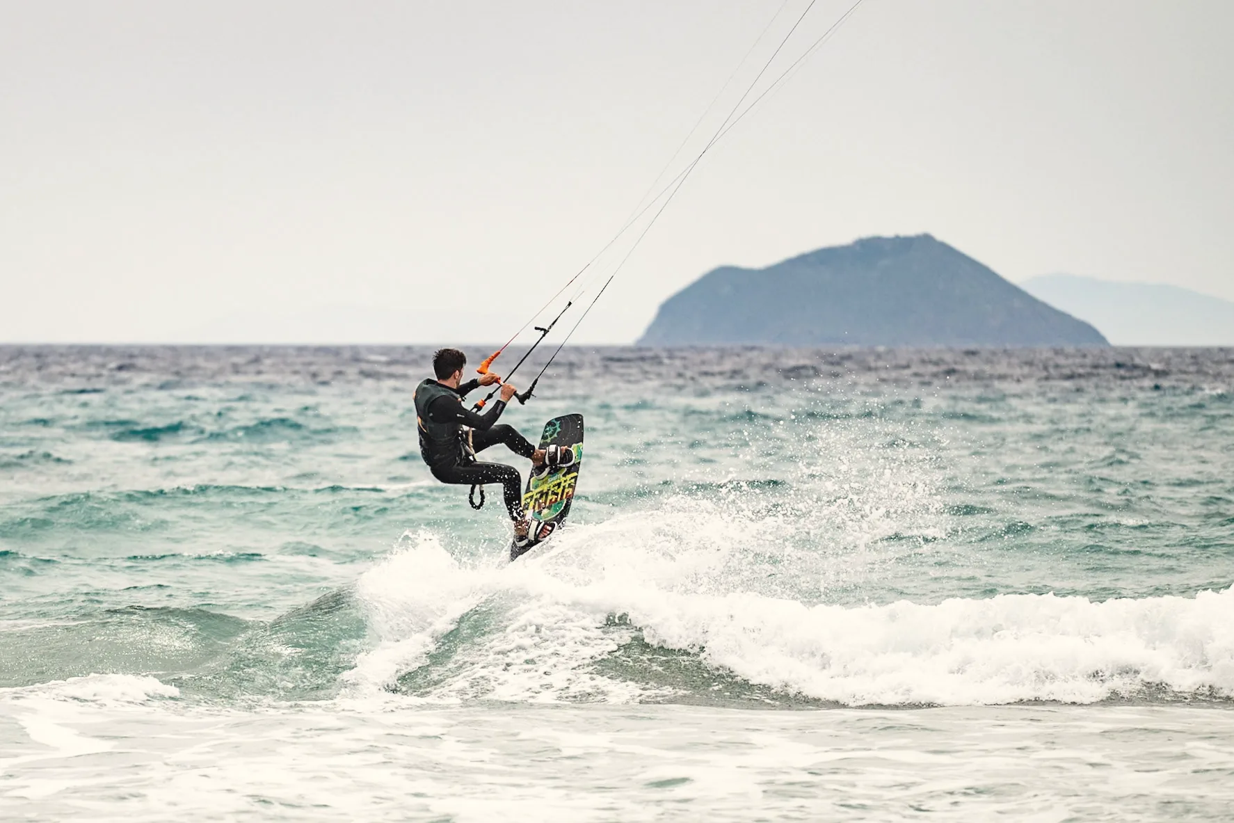 Till springt mit dem Kite über eine Welle, im Hintergrund eine Insel